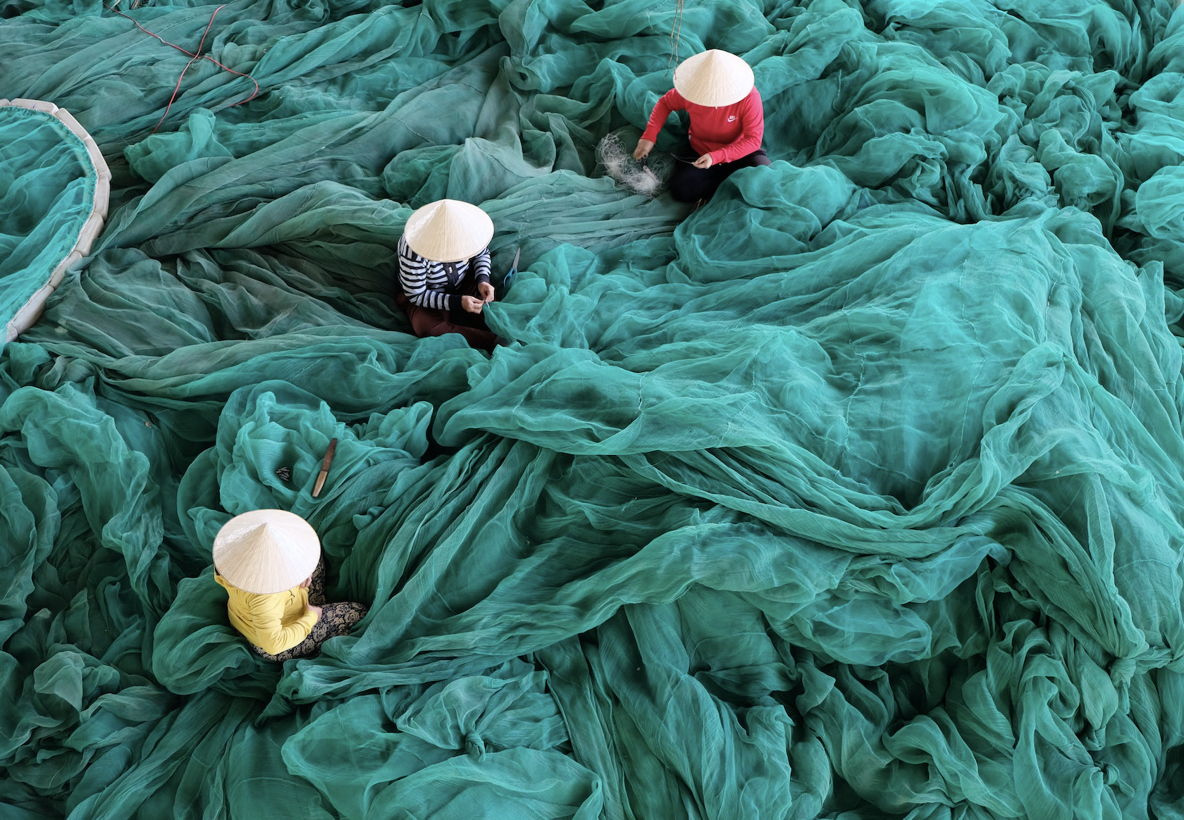 imagem de pessoas com chapéu vietnamita mergulhadas em uma grande teia de tecidos, tentando organizá-la sugerindo o trabalho de um design de soluções e experiências